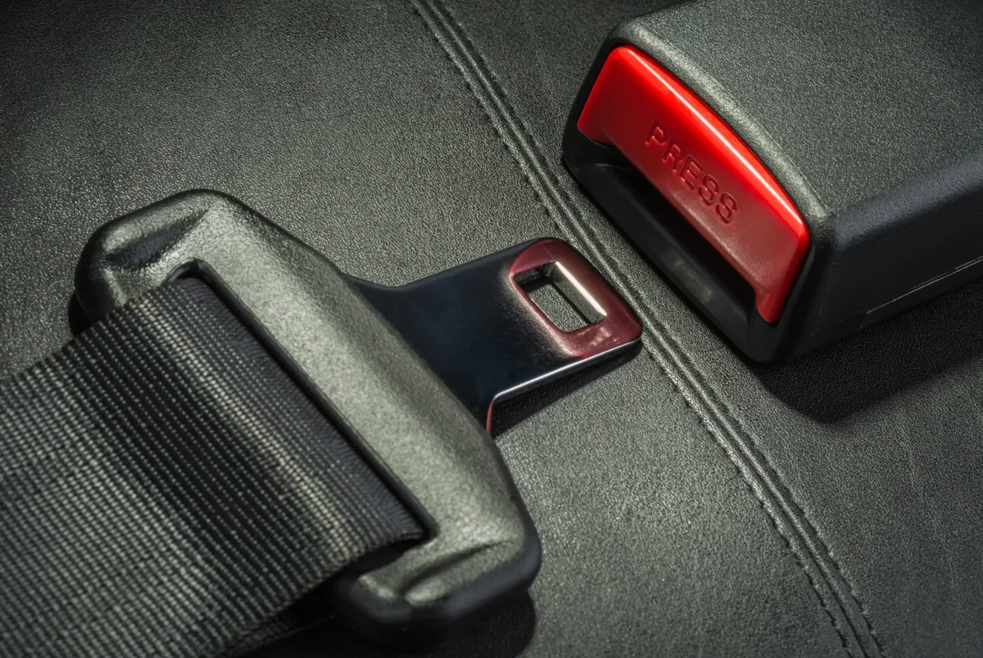 Seat belt webbing, polished tongue plate and red release buckle on a dark textured seat surface