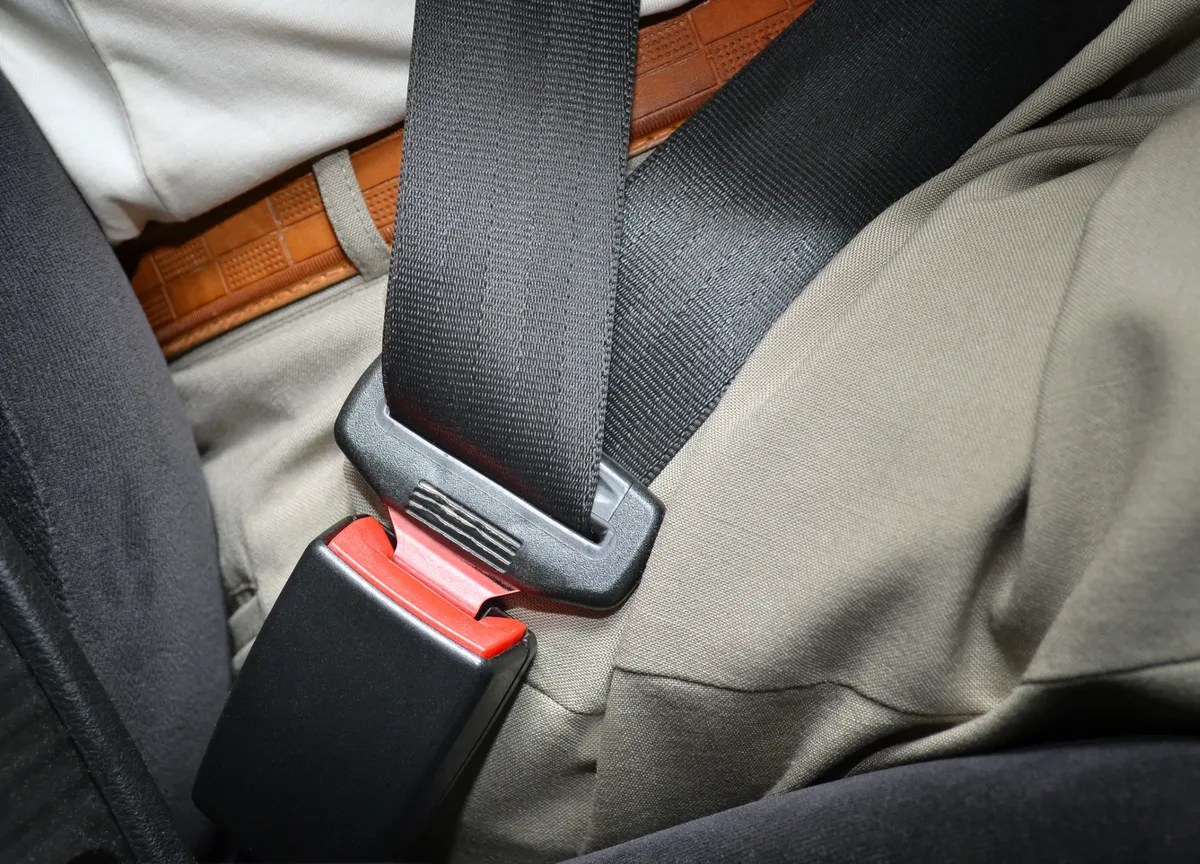 Fastened seat belt lying across the lap of a seated vehicle occupant beside the buckle