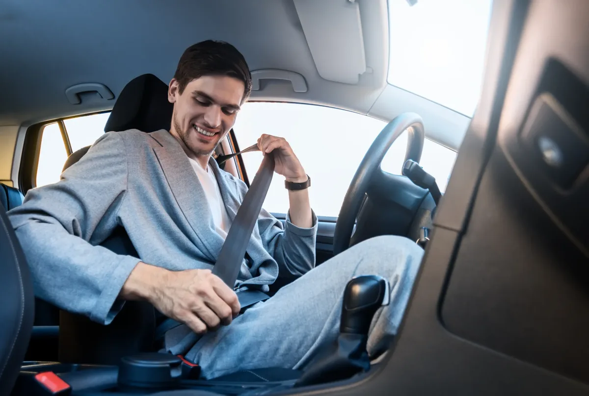 Occupant seated in a passenger car drawing the seat belt webbing across the body