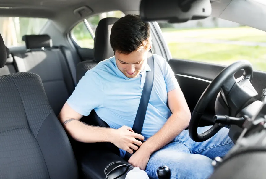Driver fastening a seat belt inside a vehicle cabin with the steering wheel in view