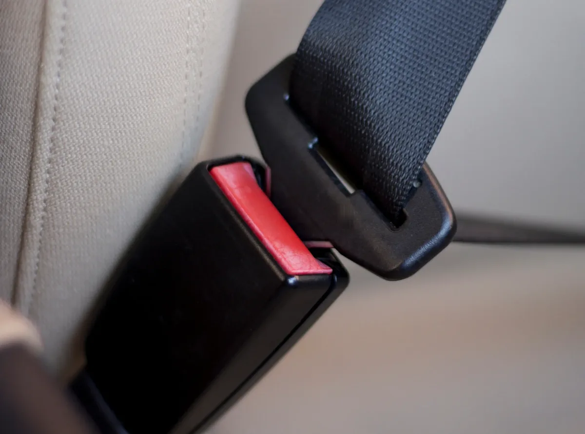 Seat belt buckle with red press release button shown alongside its mating tongue plate