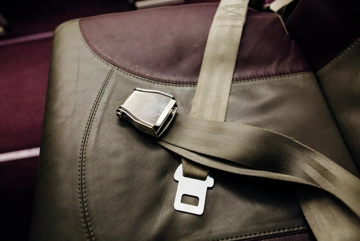 Chrome lift-latch restraint buckle and webbing fitted across an upholstered transport seat